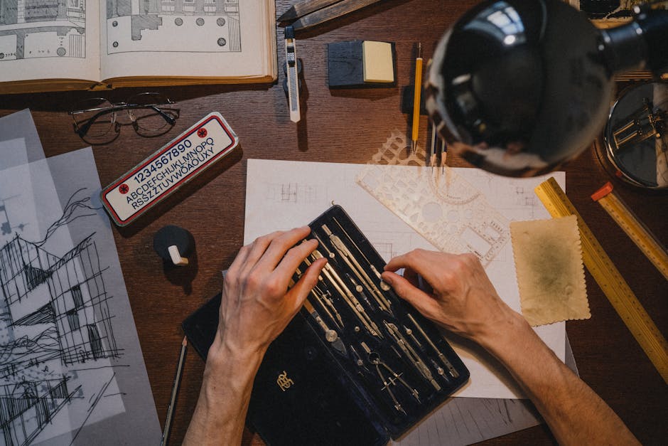 Overhead view of an architect's hands working on blueprints with drafting tools on a wooden desk.